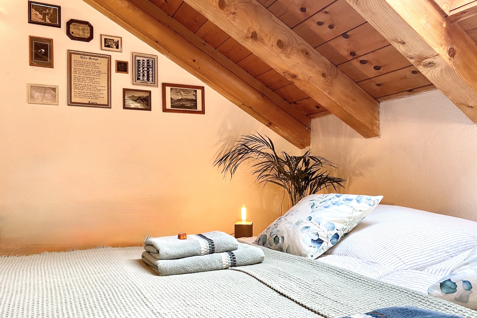 Doppelbett im Appartement Sternenblick mit dekorativer Bilderwand unter sichtbarem Holzdachstuhl